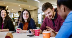 Racially mixed group of students socialising in the Library Coffee Shop (prior to social distancing measures).