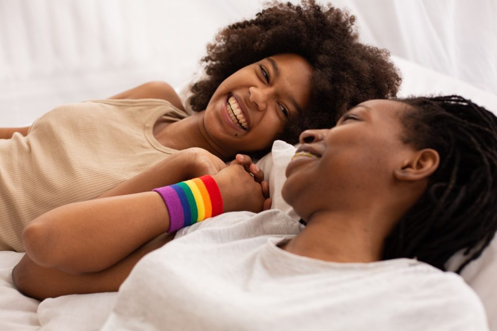 Black female couple holding hands, one wearing a rainbow wristband.