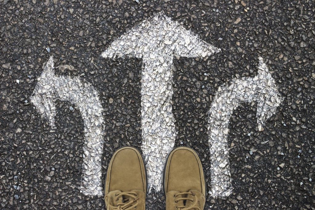 Photographic image of the ground at a person's feet, where three arrows suggest turning in one of three different directions, representing a choice point.