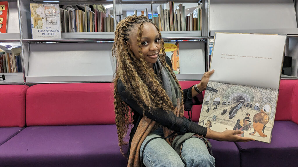 Abigail Adenaike holding up the illustrated children's book "A lion in Paris"
