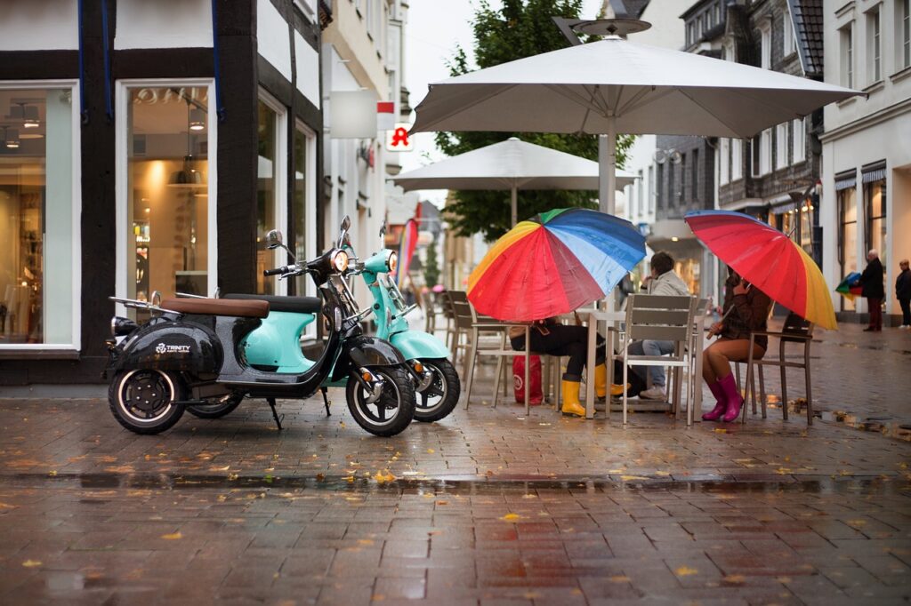 Two people sat outside cafe with rainbow umbrellas. From Pixabay - https://pixabay.com/photos/electric-scooter-scooter-street-4983759/