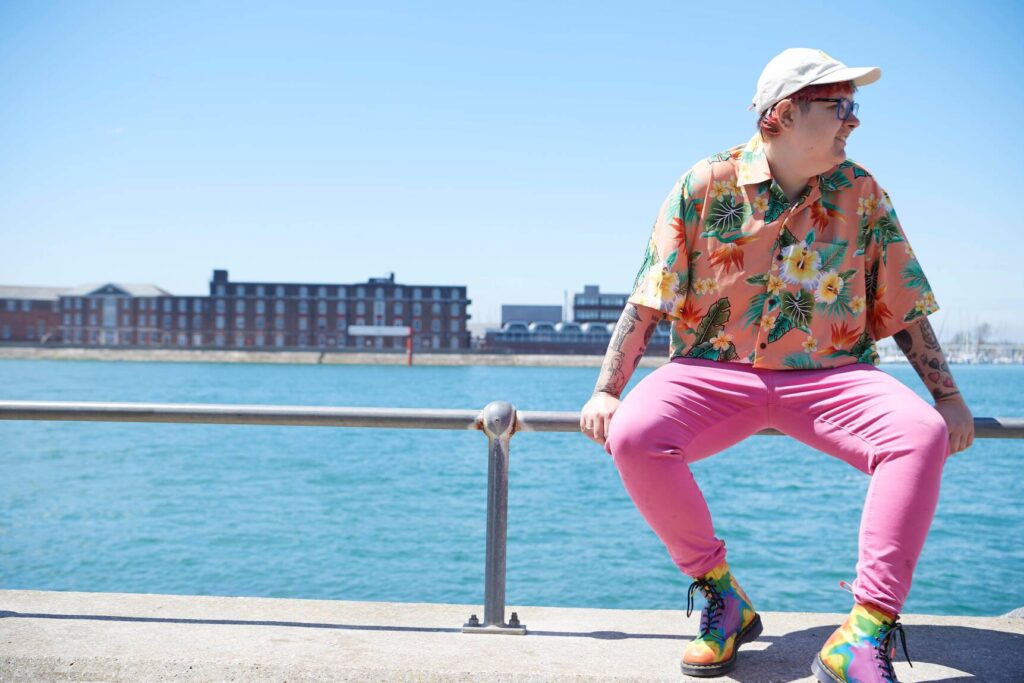 Woman wearing brightly coloured clothes perched on a railing overlooking Portsmouth Harbour